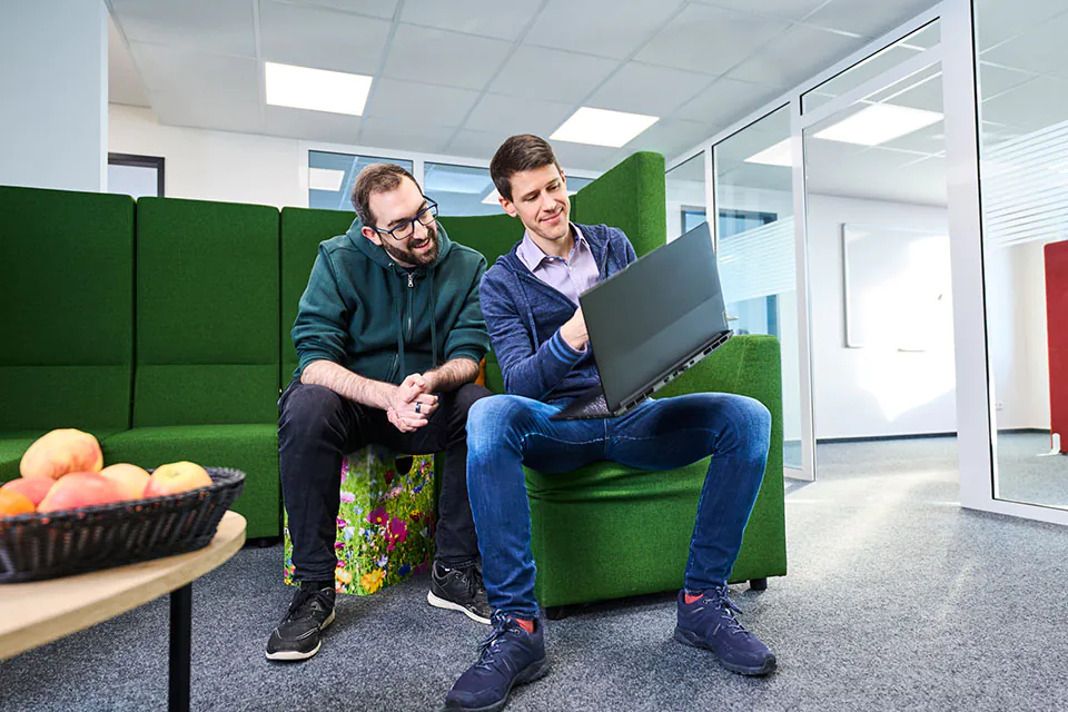 Fabian und Jan sitzen auf grünen Sofa mit einem Laptop